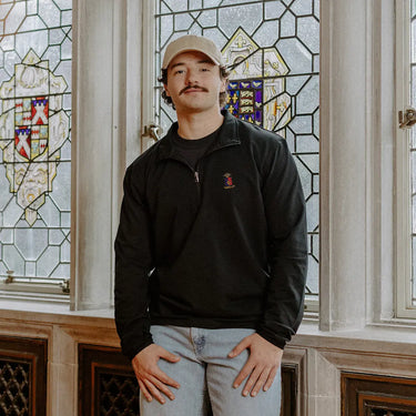 Male model wearing the black Sigma Phi Epsilon Embroidered Luxe Quarter Zip in front of stained glass windows with fraternity crests.