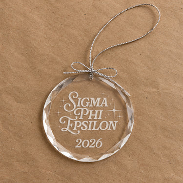 2026 Limited Edition clear glass holiday ornament featuring engraved fraternity design and silver hanging string