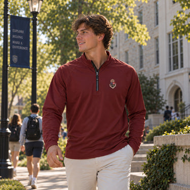 College-aged man wearing a maroon Cutter + Buck Adapt quarter zip with embroidered chest crest and khaki pants while walking outdoors on a college campus.