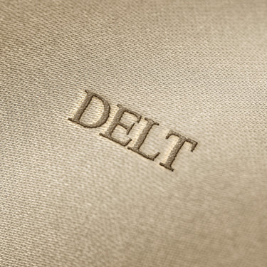 Soft beige fabric close-up showing a smooth, heavyweight knit texture with gentle folds and subtle draping.