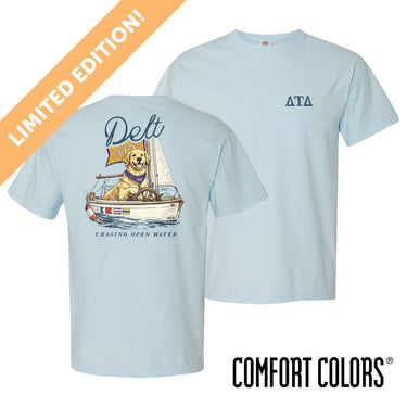 Light blue Comfort Colors t-shirt shown front and back; front features small Greek letters on the left chest, back displays a golden retriever sailing a boat with script text above and “Chasing Open Water” below.