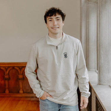 Male model wearing the smoke-colored Lambda Chi Alpha Embroidered Luxe Quarter Zip with crest embroidery, standing by a window in a formal setting.