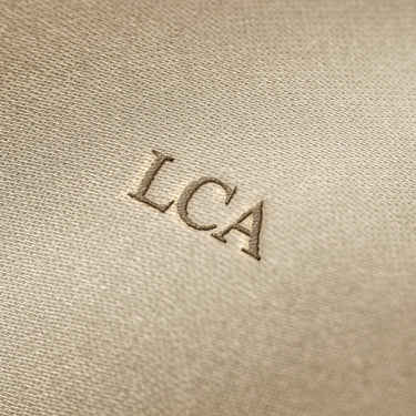 Soft beige fabric close-up showing a smooth, heavyweight knit texture with gentle folds and subtle draping.
