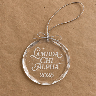 2026 Limited Edition clear glass holiday ornament featuring engraved fraternity design and silver hanging string