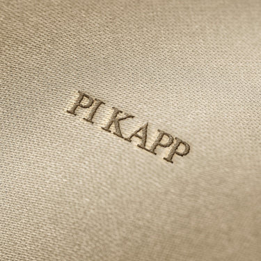 Soft beige fabric close-up showing a smooth, heavyweight knit texture with gentle folds and subtle draping.
