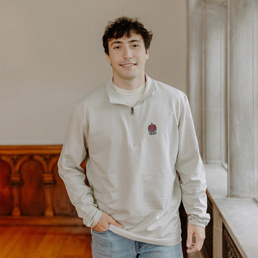 Male model wearing the smoke-colored Tau Kappa Epsilon Embroidered Luxe Quarter Zip with crest embroidery, standing by a window in a formal setting.