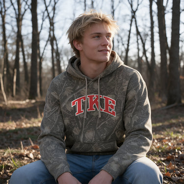 TKE Deadwood Camo Hoodie featuring an all-over woodland camouflage print, red and white arched Tau Kappa Epsilon lettering, drawstring hood, and kangaroo pocket.