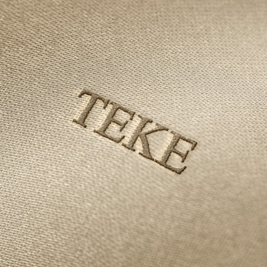 Soft beige fabric close-up showing a smooth, heavyweight knit texture with gentle folds and subtle draping.
