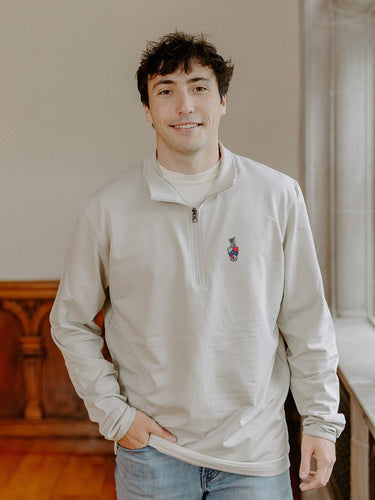 Male model wearing the smoke-colored Beta Theta Pi Embroidered Luxe Quarter Zip with crest embroidery, standing by a window in a formal setting.
