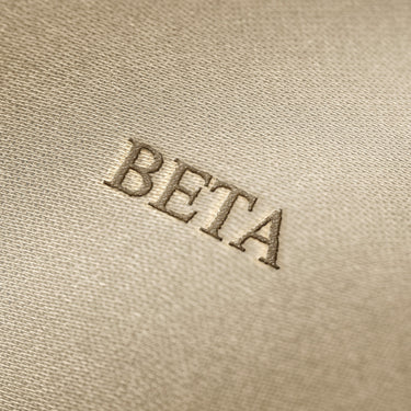 Soft beige fabric close-up showing a smooth, heavyweight knit texture with gentle folds and subtle draping.