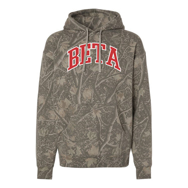 College-aged male wearing the fraternity Deadwood Camo Hoodie with red and white Beta Theta Pi lettering, seated outdoors in a wooded setting.