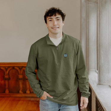 Male model wearing the pine Phi Delta Theta Embroidered Luxe Quarter Zip in front of stained glass windows with fraternity Symbols.