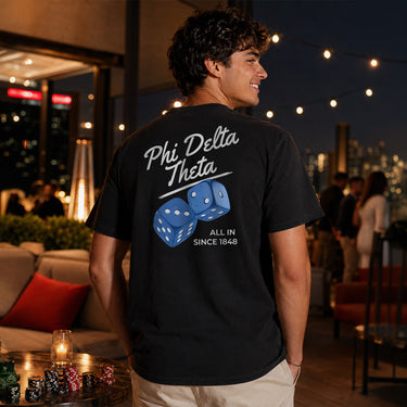 Young man standing on a dock at sunset wearing a light blue t-shirt featuring a golden retriever steering a sailboat with a flag and the phrase “Chasing Open Water” on the back.