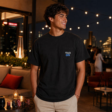 Smiling young man on a dock wearing a light blue t-shirt with small Greek letters printed on the left chest.
