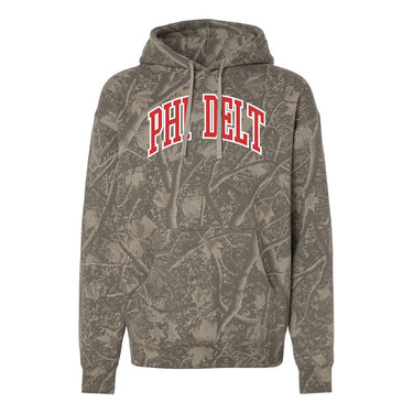 College-aged male wearing the fraternity Deadwood Camo Hoodie with red and white Phi Delta Theta lettering, seated outdoors in a wooded setting.