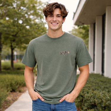 Man wearing a moss green Comfort Colors T-shirt with small chest logo detail.