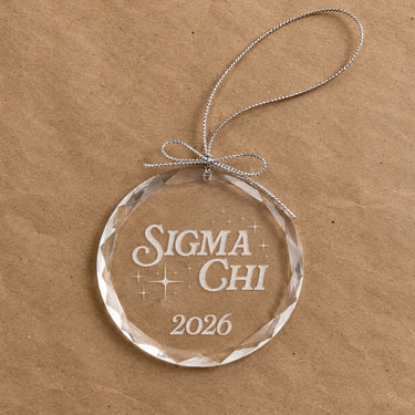 2026 Limited Edition clear glass holiday ornament featuring engraved fraternity design and silver hanging string