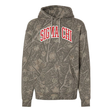 College-aged male wearing the fraternity Deadwood Camo Hoodie with red and white Sigma Chi lettering, seated outdoors in a wooded setting.