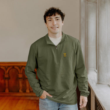 Male model wearing the pine Alpha Tau Omega Embroidered Luxe Quarter Zip in front of stained glass windows with fraternity Symbols.