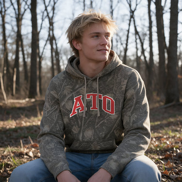 ATO Deadwood Camo Hoodie featuring an all-over woodland camouflage print, red and white arched Alpha Tau Omega lettering, drawstring hood, and kangaroo pocket.