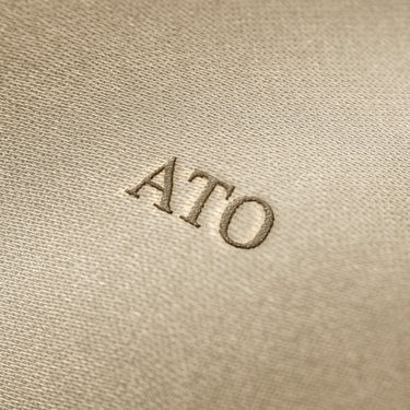 Soft beige fabric close-up showing a smooth, heavyweight knit texture with gentle folds and subtle draping.