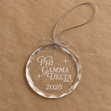 2026 Limited Edition clear glass holiday ornament featuring engraved fraternity design and silver hanging string
