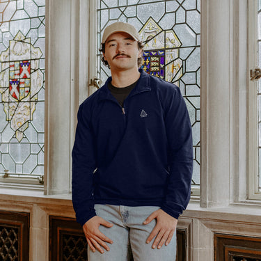 Male model wearing the navy-colored Sigma Pi Embroidered Luxe Quarter Zip with Symbol embroidery, standing by a window in a formal setting.