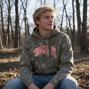 Sigma Pi Deadwood Camo Hoodie featuring an all-over woodland camouflage print, red and white arched Sigma Pi lettering, drawstring hood, and kangaroo pocket.
