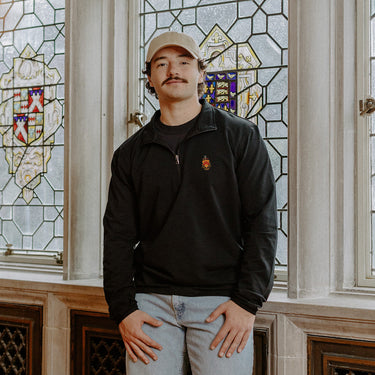Male model wearing the black Phi Kappa Tau Embroidered Luxe Quarter Zip in front of stained glass windows with fraternity crests.