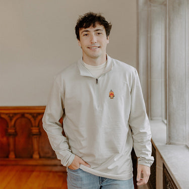Male model wearing the smoke-colored Phi Kappa Tau Embroidered Luxe Quarter Zip with crest embroidery, standing by a window in a formal setting.