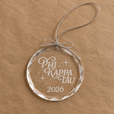 2026 Limited Edition clear glass holiday ornament featuring engraved fraternity design and silver hanging string