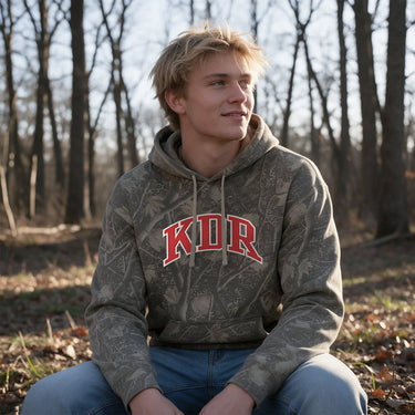 KDR Deadwood Camo Hoodie featuring an all-over woodland camouflage print, red and white arched Kappa Delta Rho lettering, drawstring hood, and kangaroo pocket.