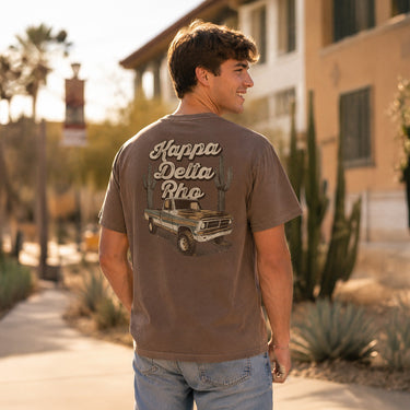Model wearing the Desert Highboy Tee from the back, showing the Kappa Delta Rho vintage truck and cactus graphic in an outdoor campus setting.