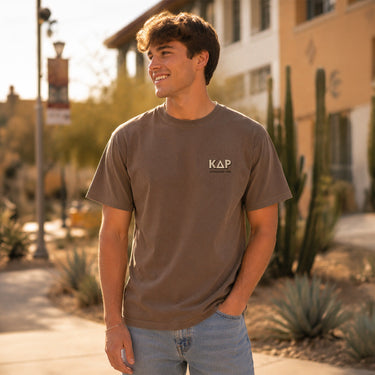 Model wearing the Desert Highboy Tee from the front, featuring a small Kappa Delta Rho chest graphic on a garment-dyed brown Comfort Colors shirt.