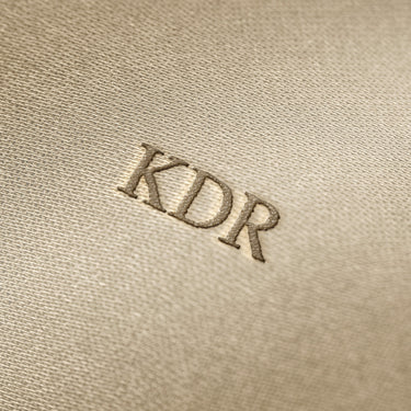 Soft beige fabric close-up showing a smooth, heavyweight knit texture with gentle folds and subtle draping.