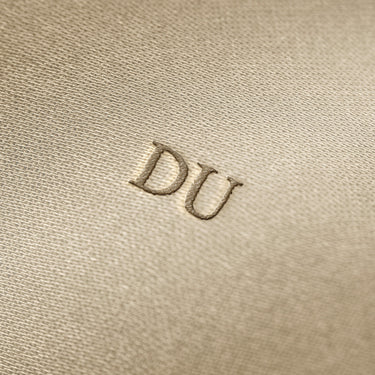 Soft beige fabric close-up showing a smooth, heavyweight knit texture with gentle folds and subtle draping.
