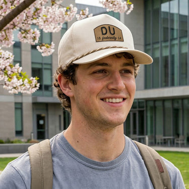 College-aged man wearing a cream fraternity rope hat outdoors on campus, showcasing classic Greek life style and everyday collegiate fashion.