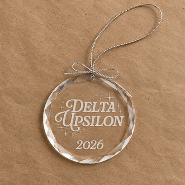 2026 Limited Edition clear glass holiday ornament featuring engraved fraternity design and silver hanging string
