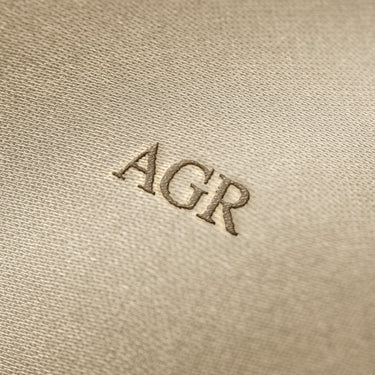 Soft beige fabric close-up showing a smooth, heavyweight knit texture with gentle folds and subtle draping.