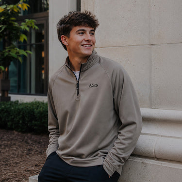 College-aged man wearing the Mushroom Cutter & Buck Adapt quarter-zip with black embroidered Delta Sigma Phi Greek letters outdoors on campus.
