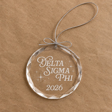 2026 Limited Edition clear glass holiday ornament featuring engraved fraternity design and silver hanging string